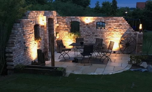Beleuchtete Natursteinmauer mit Sitzplatz am Abend